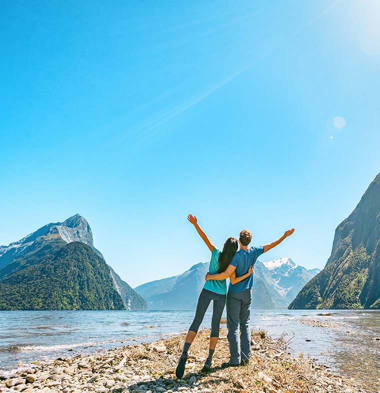 Outdoor couple happy with arms outstretched in Milford Sound New Zealand in nature enjoying active outdoor lifestyle hiking in Milford Sound New Zealand by Mitre Peak in Fiordland